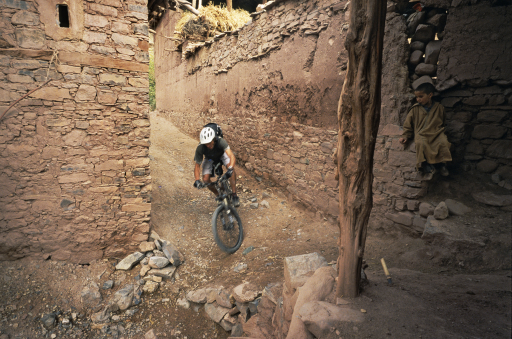 <span style='font-size:12px'>Riding through the villages of the Atlas mountains means always having an audience, even if the audience is shy. Bikes are rare here, sights of bikes like Guillaume's Enduro even rarer.</span><br><br>The reward for our labor is a 600 meter downhill. We attack it with vigor, snaking down bits of singletrack on the way and in a fraction of the time it took to climb the pass we find ourselves pulling up to a halt in Amziri, listed in our guidebook as the most remote village in the High Atlas. Through the enveloping dusk we meander among the locals, all dressed in colorful embroidered dresses and headwear, before locating the solitary gite. It's the most basic place we've ever had the dubious pleasure in staying in, period. The bathroom resembles a 1980's Turkish prison cell, and for once I'm glad of the absence of electric light in the room. Berber dialect is the only language spoken here and over candlelight my companions dine on sinuousy meat while I stave of my vegetarian hunger with biscuits. It's a character building experience. The evening is short, the climb has seen to that, and for that I'm not unhappy. Tomorrow is a new day, another ride with a different set of challenges and rewards. When plans come together it can be a rewarding feeling. When they fall at a hurdle it can be a mental and physical challenge. Setting out on a trip like this takes certain courage: the courage to leave behind the comforts of home, to leave the security of knowing what's coming next, but the rewards are immense. The very next day we would find our planned sixty kilometers of twisting singletrack reduced to fifteen kilometers of hard slog and repeated river crossings, the trail having been washed away by the previous week's flooding. It's a day of hard earned dried fruit stops, but one that terminates in a comfy bed in a village of friendly people and excitable kids. Guillaume was right; all we needed was a bike and a backpack. In exchange, our reward was an insight into a different world, one that we got to ride our bikes up, down and through, and even rail a few berms along the way.