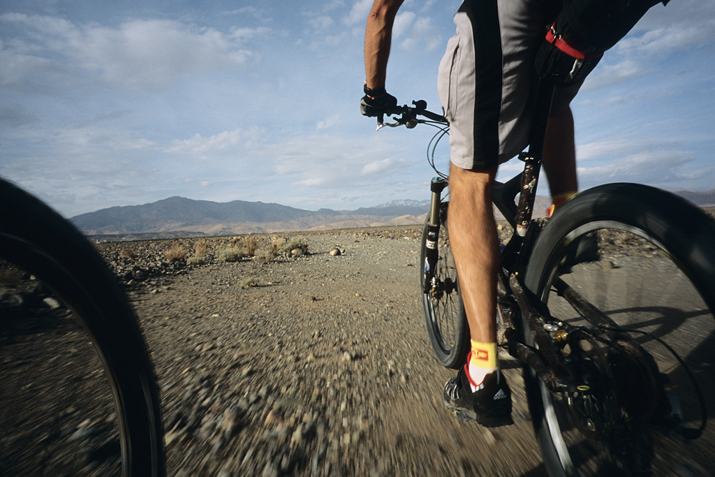 <span style='font-size:12px'>Once out of Ouarzazate we had the pleasure of recrossing the plateau to the south of the atlas -an easy spin- before starting what would inevitably be the mother of all climbs back up into the mountain, and over our 2700m pass next day.</span><br><br>Behind us is desert, and in front the majestic snowy peaks of high mountains. At the village entrance is an uninspiring looking gite, but day three weariness persuades us to pedal by in search of something slightly more salubrious. Berber Arabic is replacing French as the language spoken but as we sip on another cup of sugar solution disguised as tea, we can decipher enough to know that there is only one hostel in town. Tired and with darkness closing in we U turn and head back to the gite we already passed. I should of course know better than to judge a book by its cover, or a gite by the state of its rendering. Inside we find a comfortable room festooned with blankets and rugs and a tray of tea and the almonds laid out to greet us. A tumble of kids, eight of them, ranging from two to fourteen in age, hover at a safe distance, keeping a wary eye on us until summoning up enough courage to come closer. They're adorable of course and by the end of the evening are sitting on our laps and teaching us Berber while we help the oldest son with his French homework. Over dinner we learn the ins and outs of mud house construction and the reasoning behind having so many kids (in a country with no state pension, caring offspring are the way to survive old age). The magical night we spend in this hostel is one I'll never forget. We have a big day ahead of us including the 2700 meter pass, and set off early next morning, accompanied by the oldest son on his way to school. His bike is clanking but thanks to Guillaume's chain lube, no longer squeaking. The boy's bike is tired, the gears gave up long ago and there's a serious wobble in the back wheel, but he loves it. It's the state of all the bikes we see during our trip: overused and minimally maintained. For many villagers, the bike or the mule are the only forms of affordable independent transport and both are heavily used. On our last day a guy in a Jalaba, the archetypal, long hooded cloak, will overtake us on a creaking bike that has definitely seen better days. From the back of the evolving peloton, Mike and I will watch him reel in Guillaume and then take him at the pass to claim the polkadot jersey. His bike will be rattling and his chain rusty, while ours will sport navigation devices that are updated every five minutes by satellites. At times during our week, the feeling of 'us and them' is overwhelming, but despite the differences in lifestyle, religion and customs, our bikes repeatedly forge ties with many people we meet. They are the equivalent of carrying a cricket bat around Pakistan. The climb up the pass is spread over forty kilometers and will take us all day to conquer. For most of the day we follow a stunning V shaped valley, carved out over millenia by a river that now flows far below us. The valley is typical of the Atlas, a mountain range that has not been scooped out by glaciation and the hillsides around us radiate shades of red and brown and green.