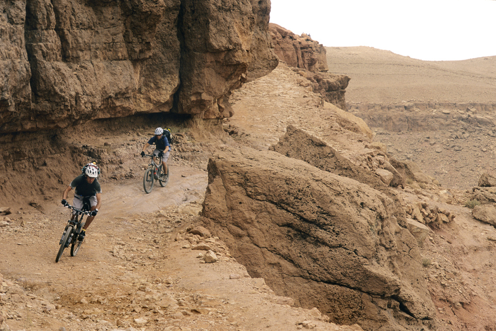 <span style='font-size:12px'>Even the jeep tracks in Morocco make fun riding. Mike and Guillaume put the hammer down on one of our rockier sections.</span><br><br>Our sleep is broken by the enigmatic early morning call to prayer, the unmistakable sound that punctuates trips to any Muslim country. We follow breakfast by wandering through the market, weaving between piles of vegetables and stepping over occasional discarded severed goats' hooves to stock up on dried fruit for the day's ride ahead of us. Above our heads it looks like a storm may be brewing, but no one can tell us if it will rain. The weather forecast here is