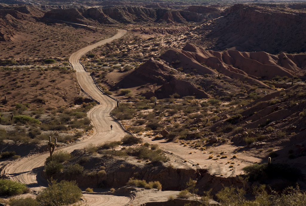 <span style='font-size:12px'>Dramatic scenery is guaranteed in this region. A traverse of the Cardones park on the only jeep track gave us the starting point for finding the few singletrack, river beds and fun features to fill a morning playing before fleeing back to town for well earned shade, pastries and steaming mate tea.</span><br><br>If you're looking for spares look no further than the local bike shop in the town of Cachi. It might not be able to service your Rockshox Revelations, but it does have an abundant and essential supply of puncture patches. You will be grateful.</span><br><br>Our 'trail' then is a meandering flat riverbed carved out between incredible red rock formations from behind which I half expect Wil-E-Coyote to leap brandishing a stick of ACME branded dynamite. We start riding tentatively, expecting our front wheels to soon be bogged down or wash out in sand, but are surprised to find the surface baked hard instead. It's almost like the river suddenly stopped and its tumbling sand and mud instantly frozen in time, which is pretty much what has happened, as soon as the sun came out. Here rain falls infrequently and when it does it comes as flash floods. As quickly as it comes the water recedes and the deposited sand formations are soon baked hard by a searing sun. Gaining confidence in our front wheels' traction we start to weave our bikes about zig-zagging between stranded boulders and hopping on and off raised platforms and railing natural berms in the river bank. Everything is baked rock-hard making it seem like we're riding a concrete BMX park at times. Eventually, with a couple of condors ominously circling overhead we reach the head of the once-flowing river where it emerges from a narrowing canyon carved out of the hillside over thousands of years. We ride the canyon as far as we can until it is too narrow to fit our bars through before being forced to U-turn. Needless to say with gravity on our side, the return leg gets more of a hammering than the climb, and we immerse ourselves in an almost pedal-free play session all the way back to the car. Truly the definition of 'trail' has just been re-written.